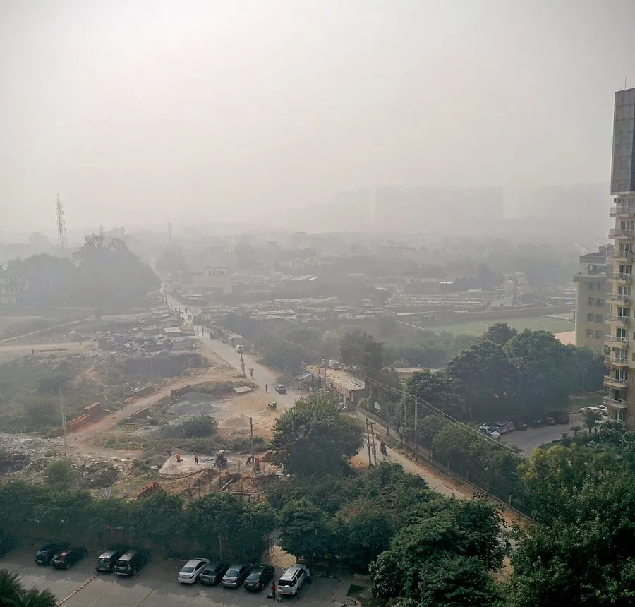 Smog over Gurgaon in November 2016, with brick stacks and sand piles on an open plot beside unpaved tracks